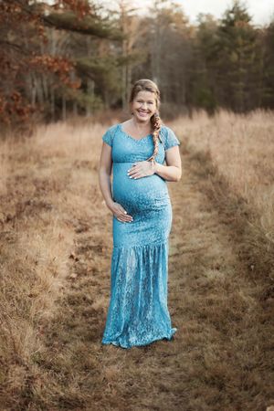 A maternity portrait session in a fall field featuring a woman in a blue lace dress.