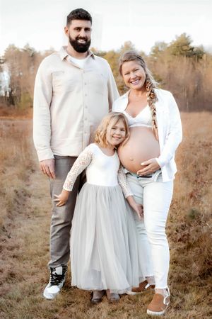 Family maternity photo session in a rustic field with coordinated white and neutral outfits.