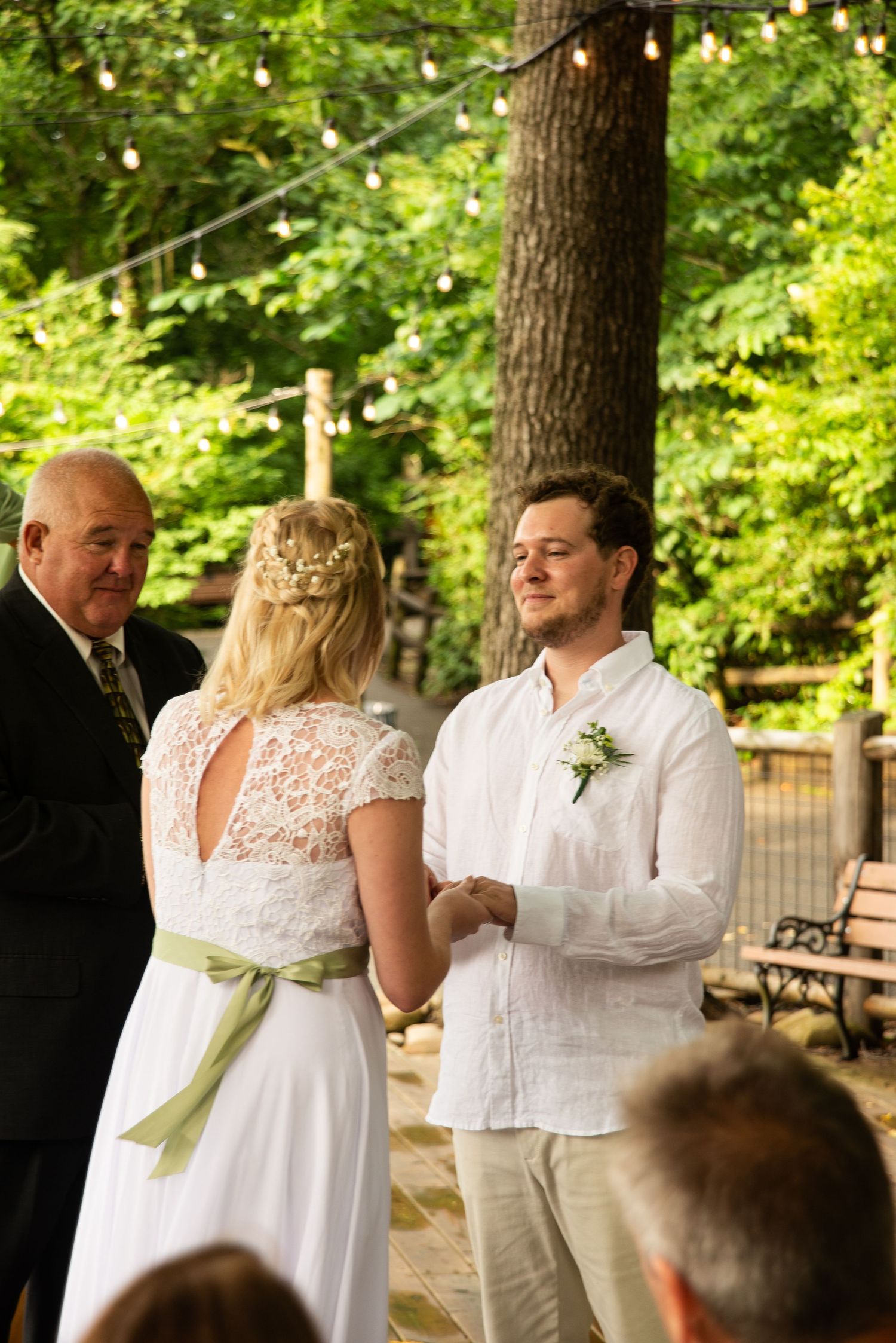 Outdoor wedding ceremony with couple exchanging vows under trees while officiant stands nearby in natural setting.