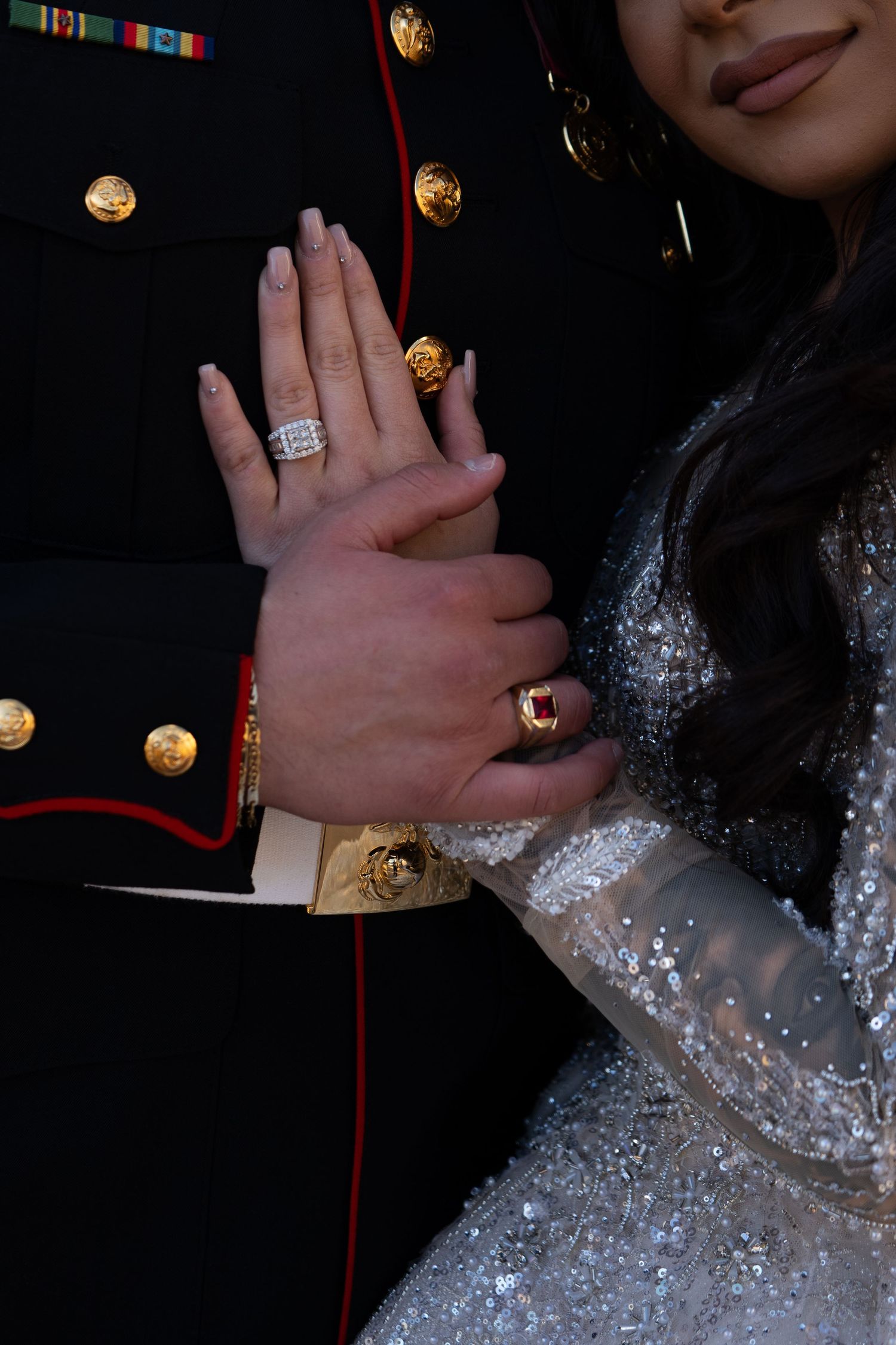 Close-up of hands showing off engagement rings against formal attire with decorative lights.