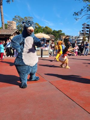 A sequence of five photos showing someone in an Eeyore character costume rolling and tumbling playfully on a brick walkway.