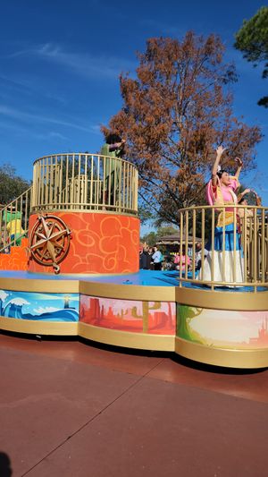A colorful curved playground wall with themed panels featuring natural designs and wooden railings against an autumn sky.