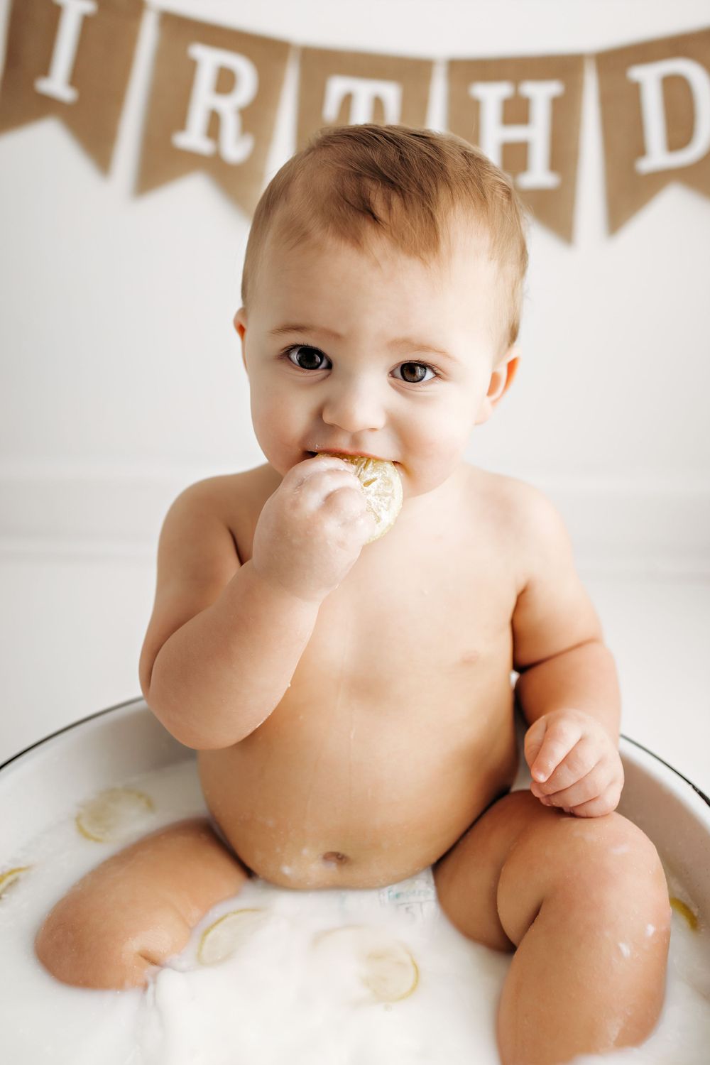 Small child enjoys birthday treats beneath a rustic banner at first birthday celebration.
