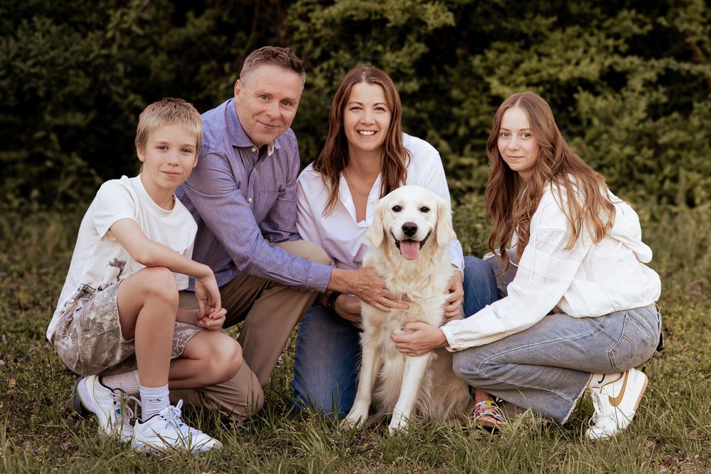 Family of four with a golden retriever dog posing together outdoors on green grass with trees in background.