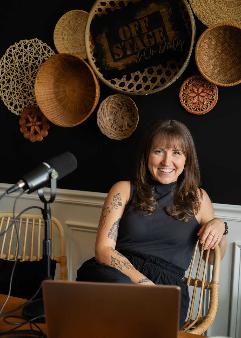 Decorative circular baskets and signs mounted on dark wall above someone seated at a workspace in casual attire.