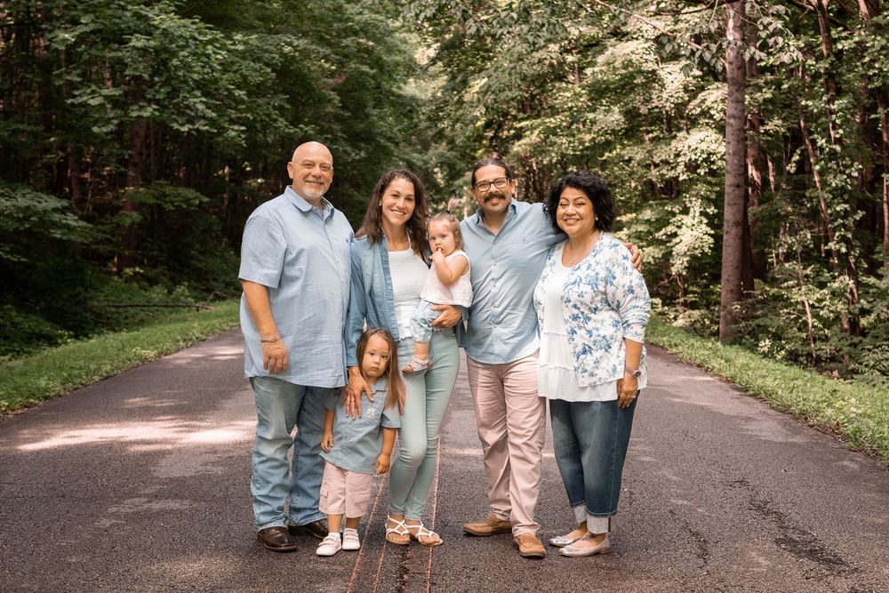 A family wearing coordinated blue and white outfits poses together outdoors in a wooded setting.