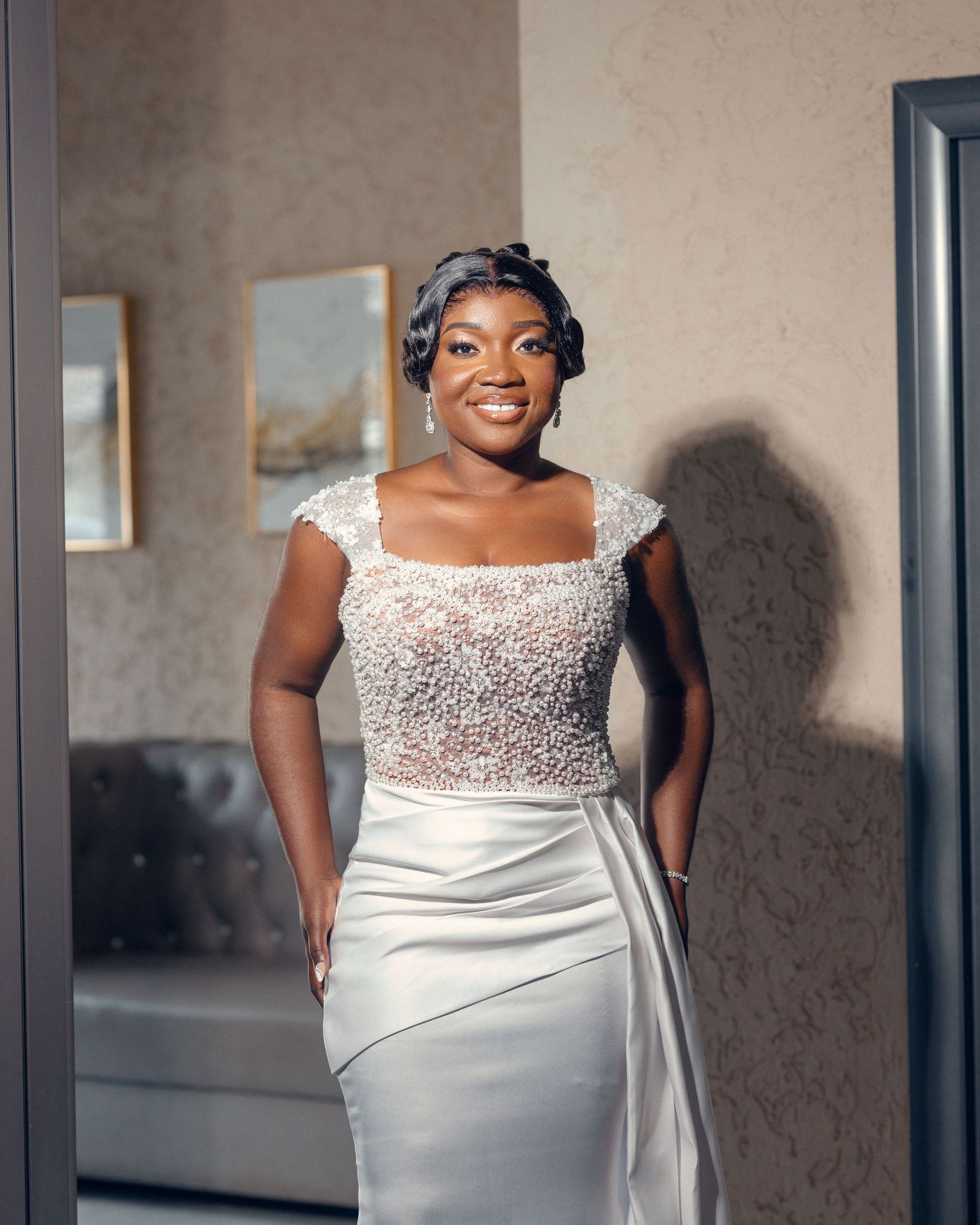 Bride wearing cap-sleeve beaded bodice gown smiles radiantly in modern interior setting.