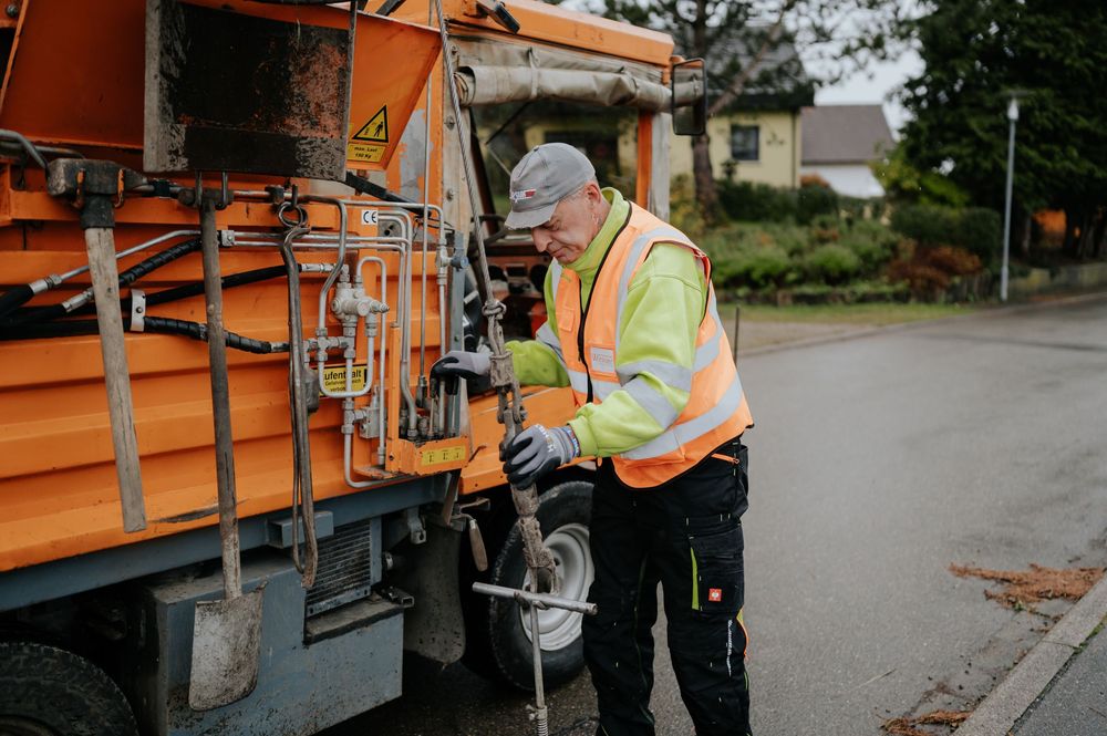 Kommunaltechniker in orangefarbener Sicherheitsweste bedient schwere Maschinen im Freien.