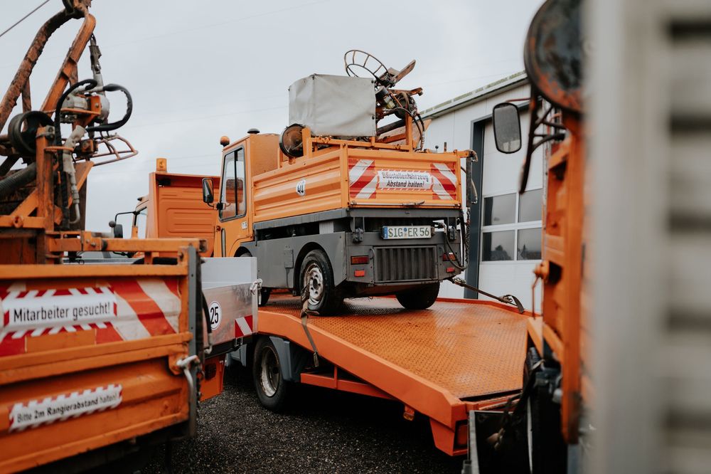 Orangefarbene Baufahrzeuge und -geräte stehen während eines Straßeninstandhaltungsprojekts auf einer Baustelle in Reih und Glied.