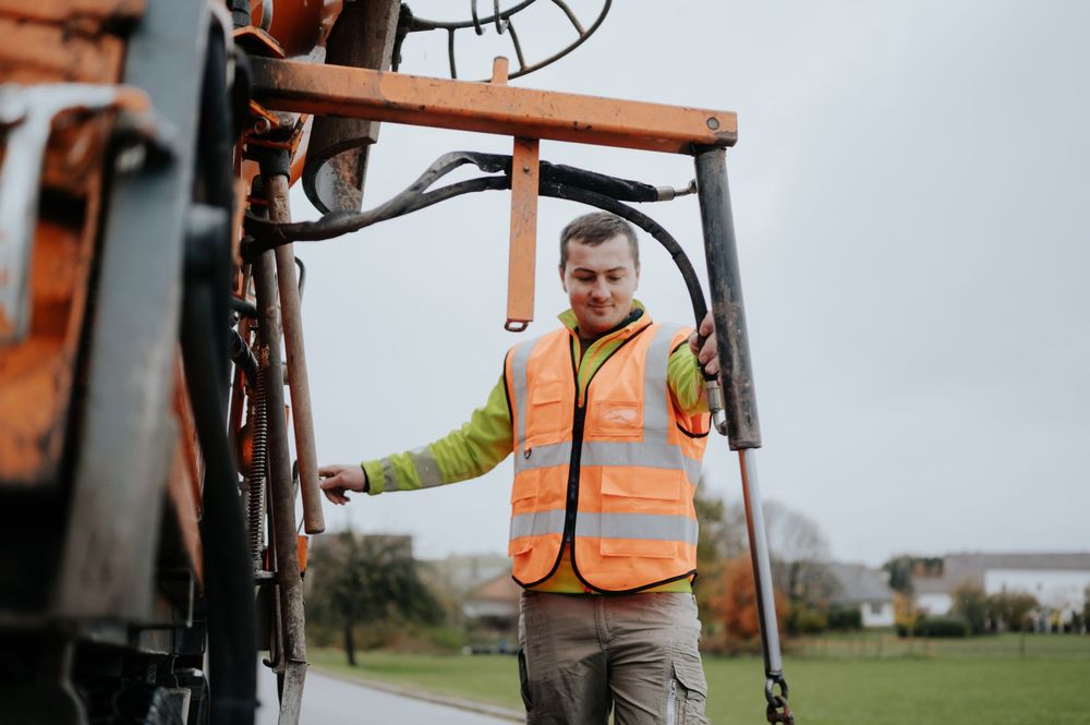 Kommunaltechniker in orangefarbener Sicherheitsweste bedient schwere Maschinen im Freien.