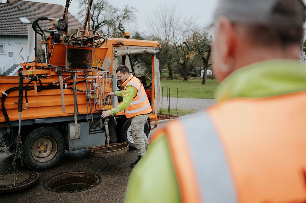 Straßenbauarbeiter bedienen eine orangefarbene Maschine während eines Autobahnbauprojekts.