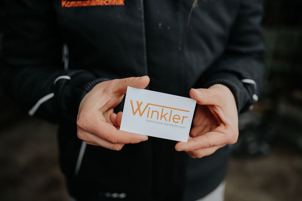 Hände, die eine weiße Visitenkarte mit minimalistischem Design vor einem dunklen Hintergrund halten.