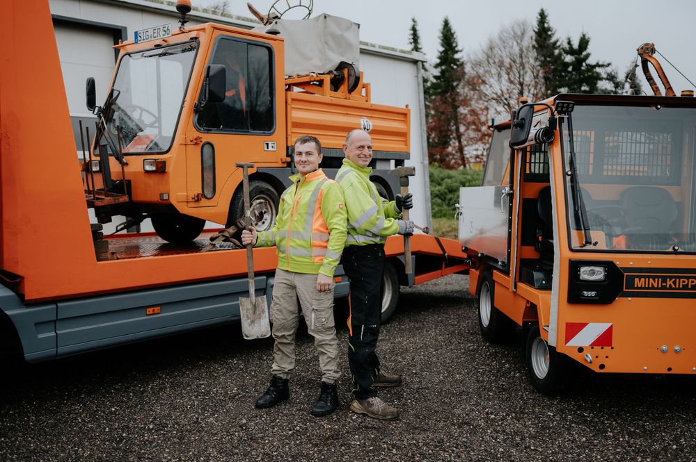 Eine Reihe orangefarbener Kommunalfahrzeuge stand in einer Reihe, und Arbeiter in gut sichtbarer Sicherheitskleidung.