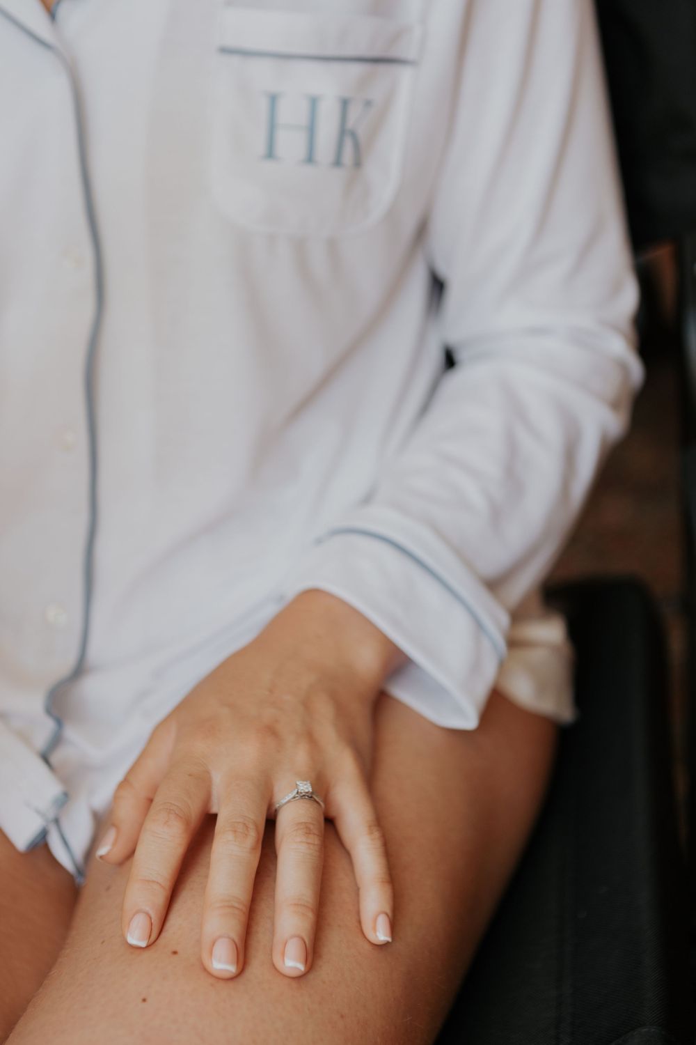Close-up of an engagement ring on a bride's hand wearing monogrammed HK white pajamas.