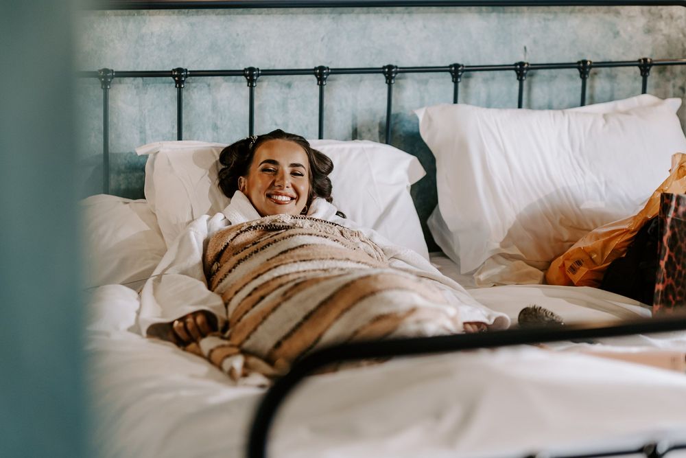 Person wrapped in white bedding smiles while relaxing in bed.