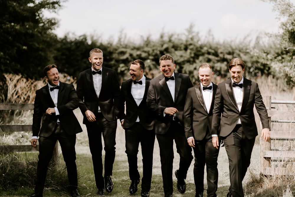 Wedding party in black tuxedos walking together outdoors in a candid moment.