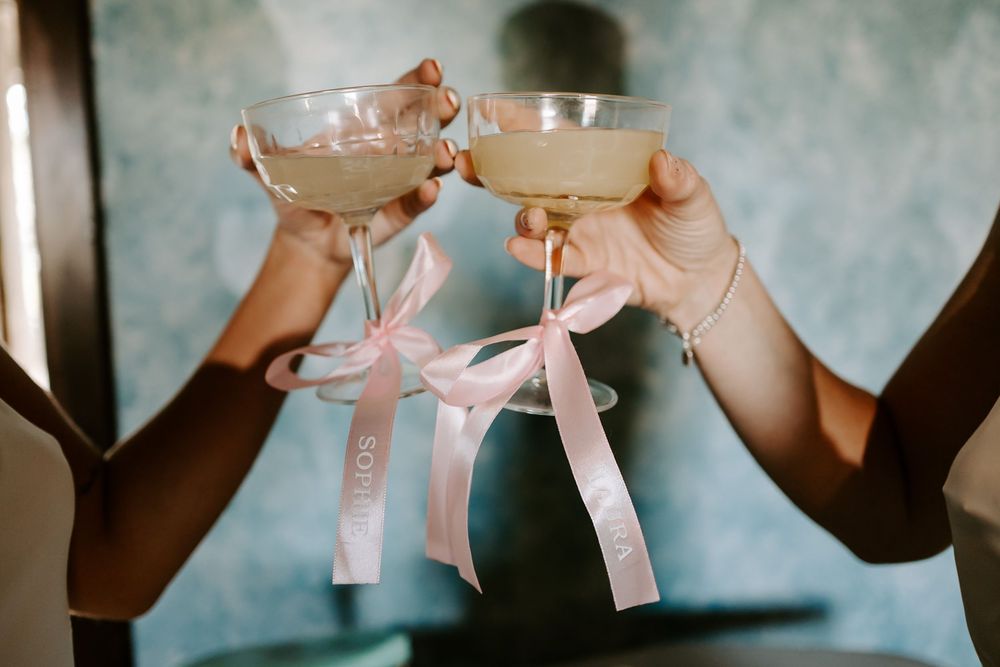 Three champagne glasses with pink bows tied around their stems sit elegantly against a gray background.