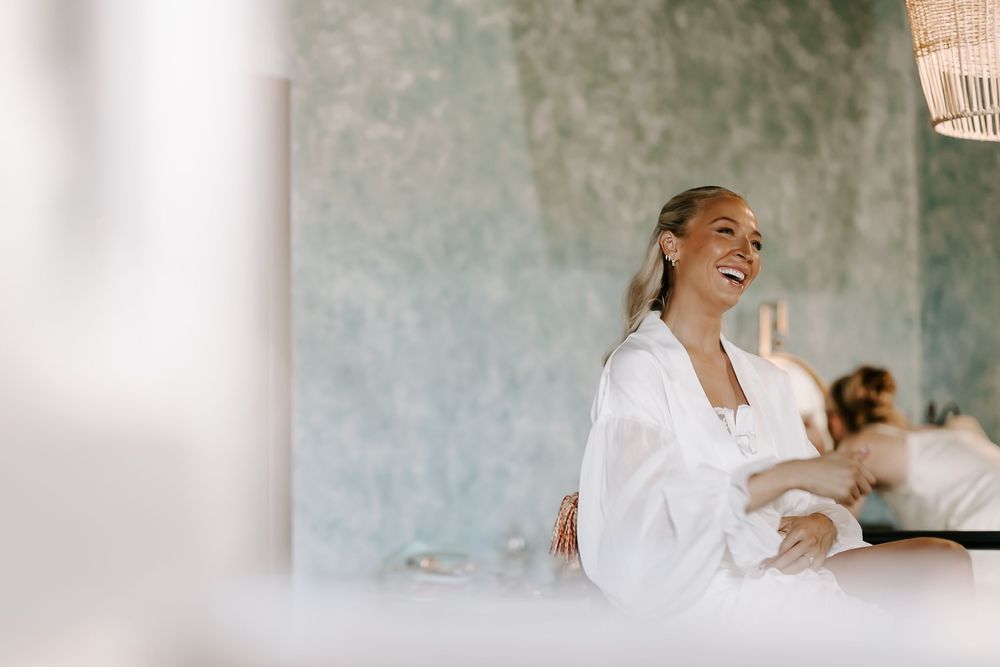 A bride in a white wedding dress and robe twirls gracefully in front of a textured gray wall.