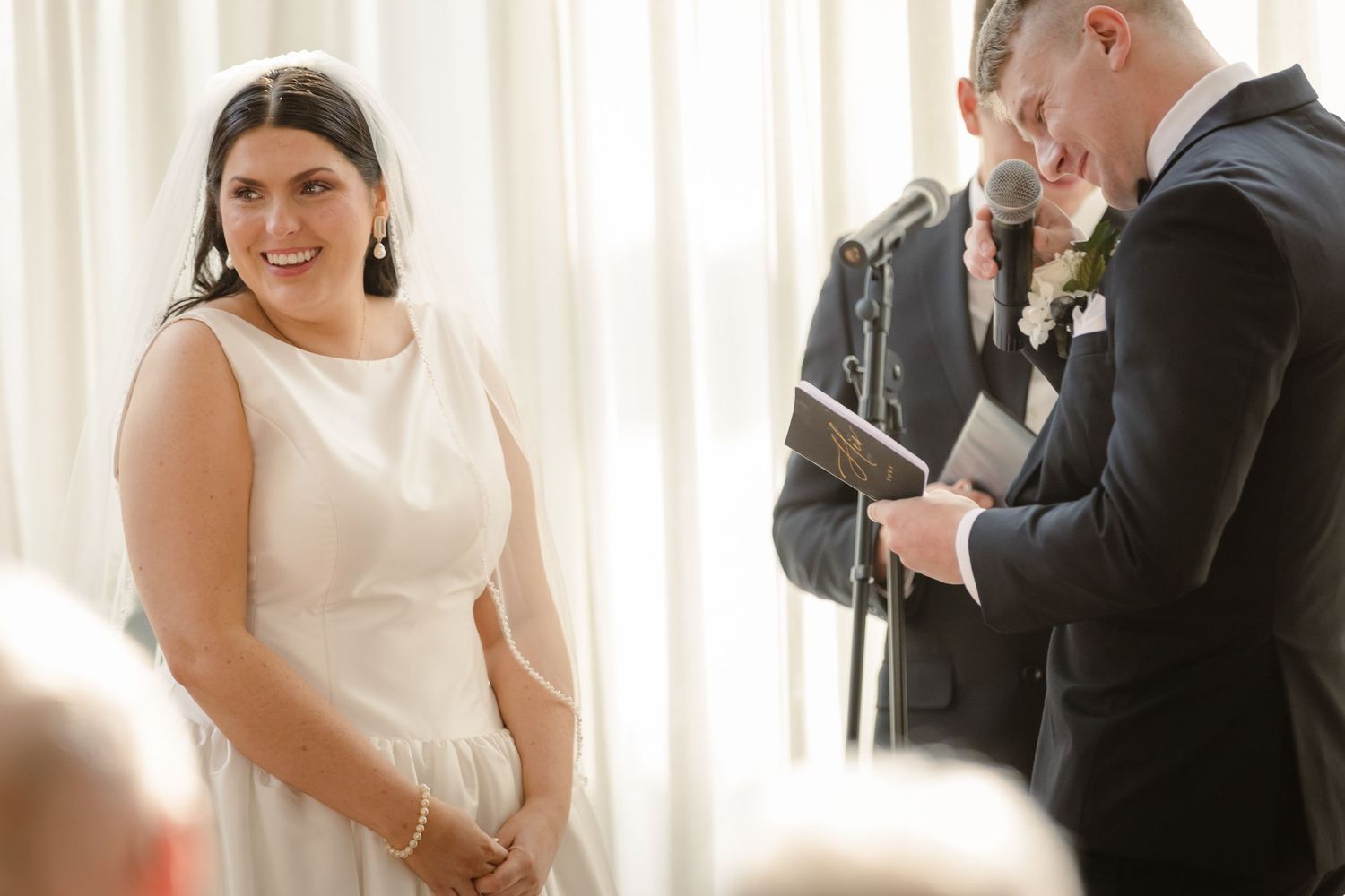 A wedding couple shares a joyful moment together during their ceremony in a bright, naturally lit room.