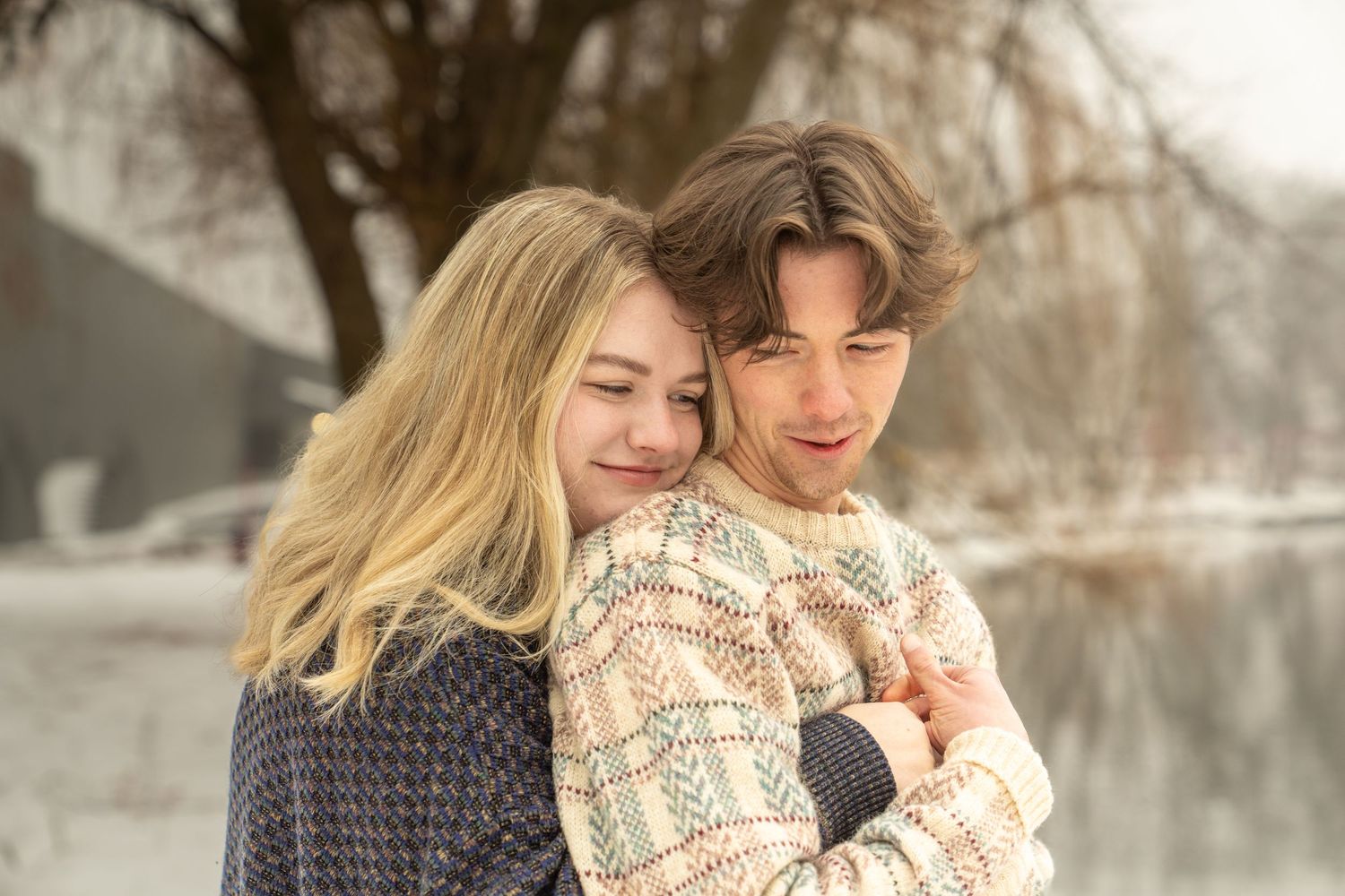 Young couple embracing warmly outdoors in a snowy winter landscape near a frozen river.