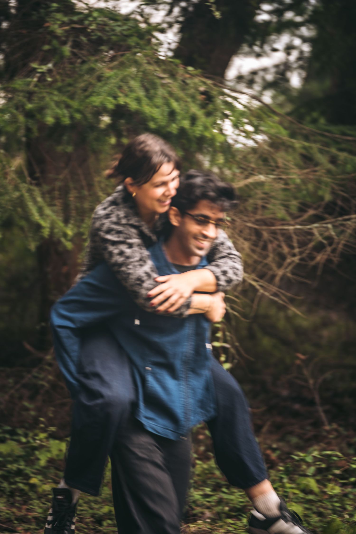 Happy couple laughing as man gives woman a piggyback ride in a lush green forest.