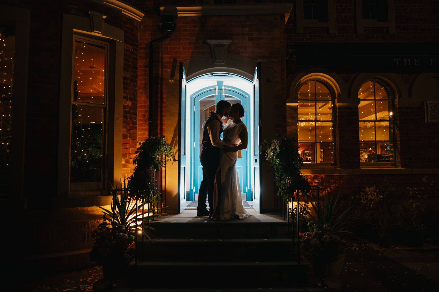 A romantic silhouette of a couple stands in a warmly lit archway at night during their wedding celebration.