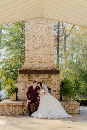 A romantic moment captured under a rustic brick pavilion with trees visible in the background.