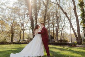 Romantic wedding couple poses together in a sunlit wooded area during autumn with golden light filtering through trees.