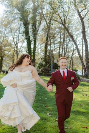 A playful wedding couple dances and twirls outdoors in a grassy area surrounded by autumn trees.