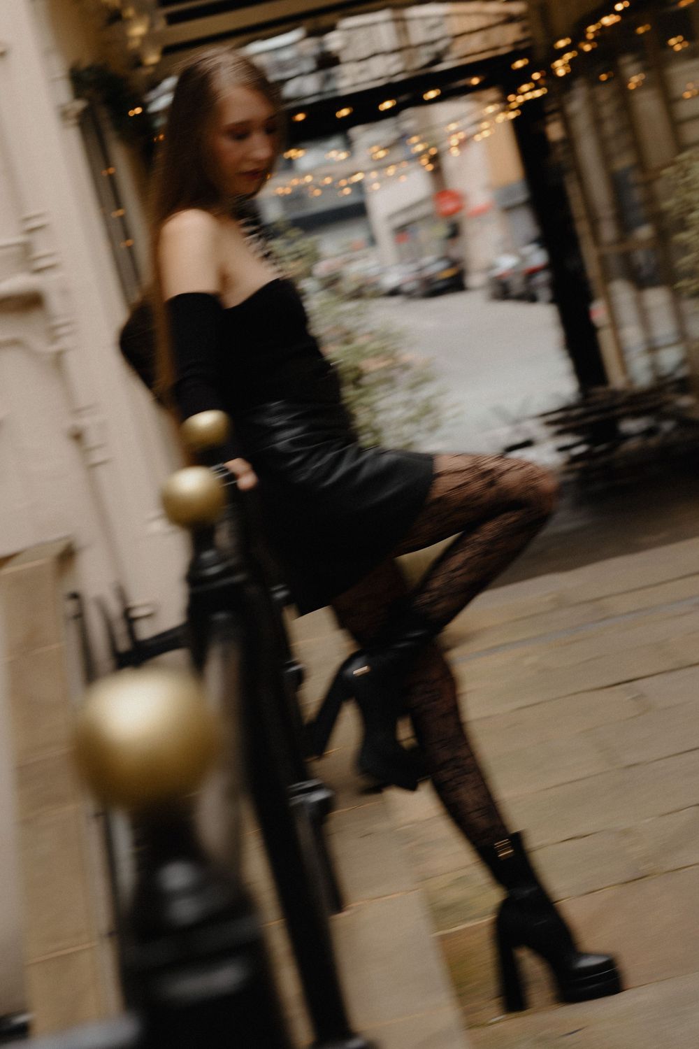 Motion blur captures someone in black clothing walking past storefronts in an urban shopping arcade.