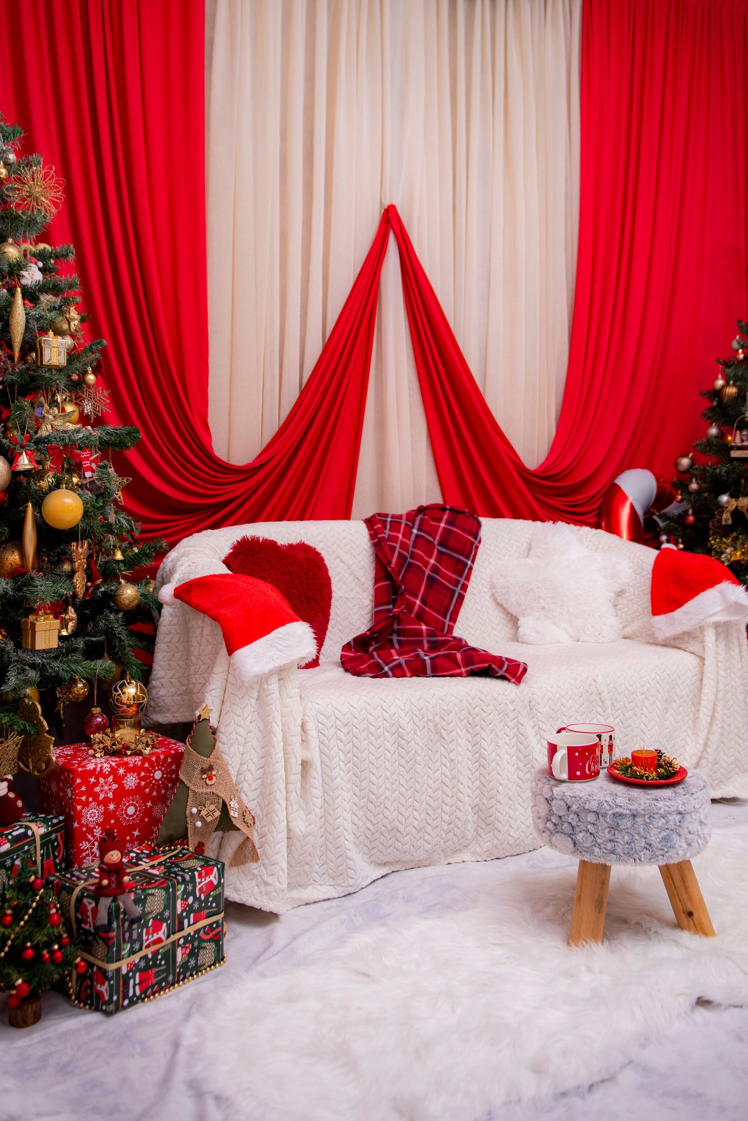Festive Christmas photo backdrop with red curtains, white couch, decorated tree and wrapped presents in winter setting.