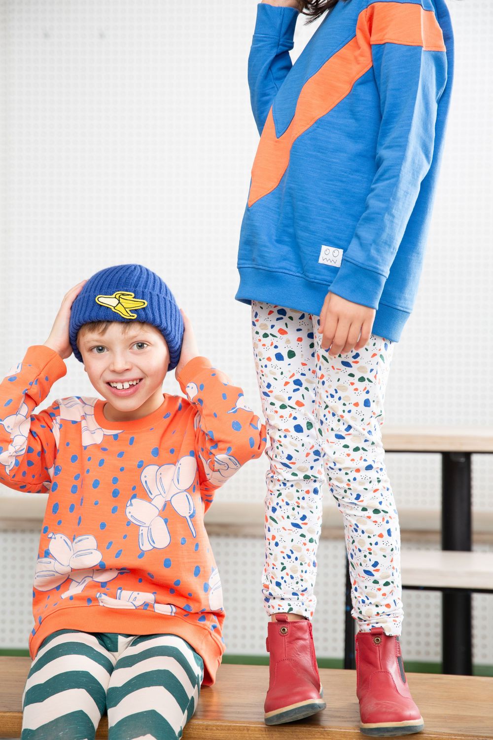 Children in bright clothing and patterned outfits playing in white studio setting.