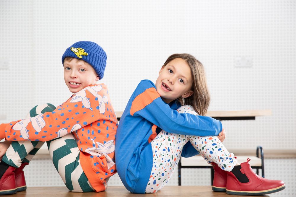 Child wearing blue hat and polka dot shirt lying playfully on wooden floor.