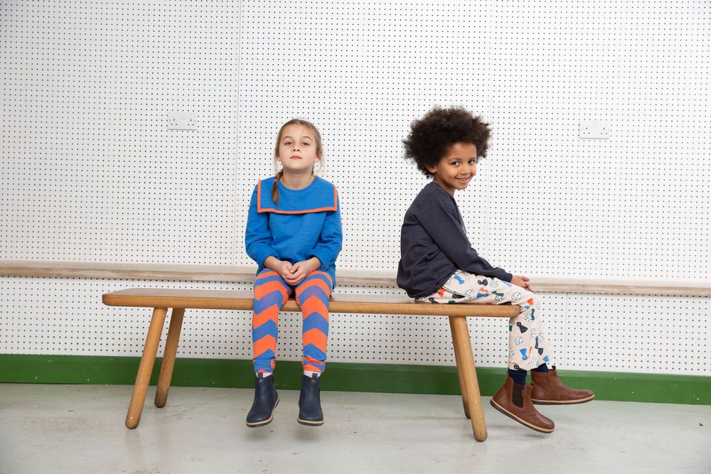 Children sitting casually on wooden bench against white wall.
