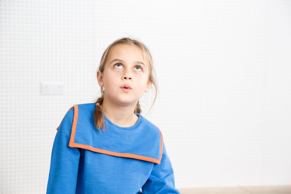 Child in bright blue outfit looking upward against white background.