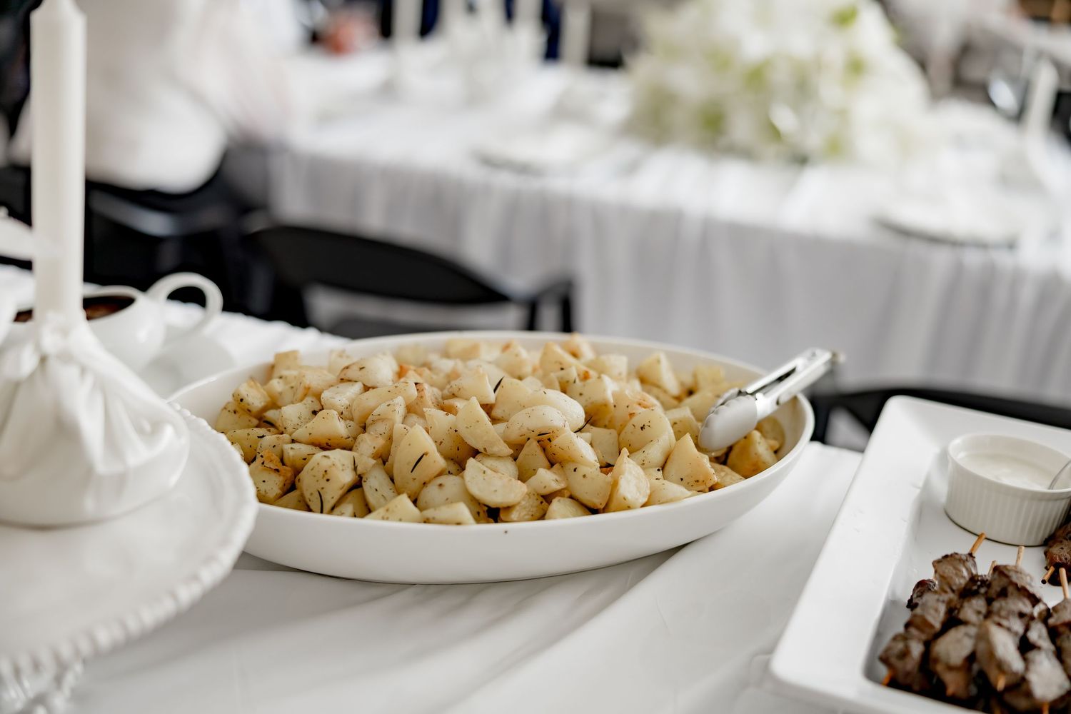 A white serving plate filled with golden brown croutons sits on a table alongside other dishes at a buffet setting.