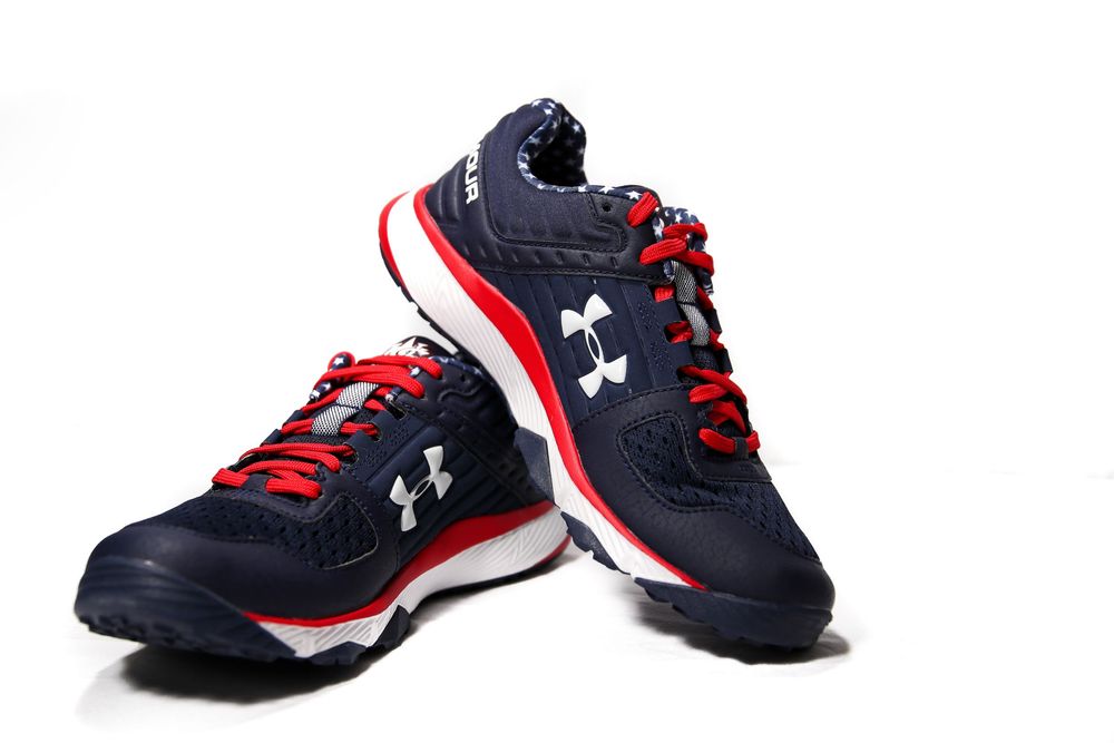 Pair of Under Armour navy blue and red lace-up baseball training athletic shoes on white background.