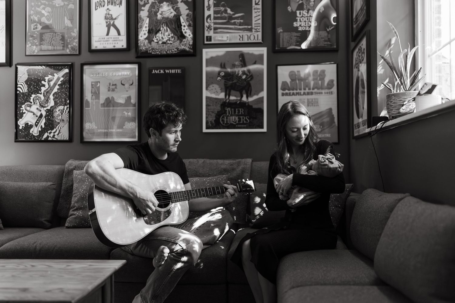 Two musicians performing with acoustic guitars in a cozy room with framed artwork.