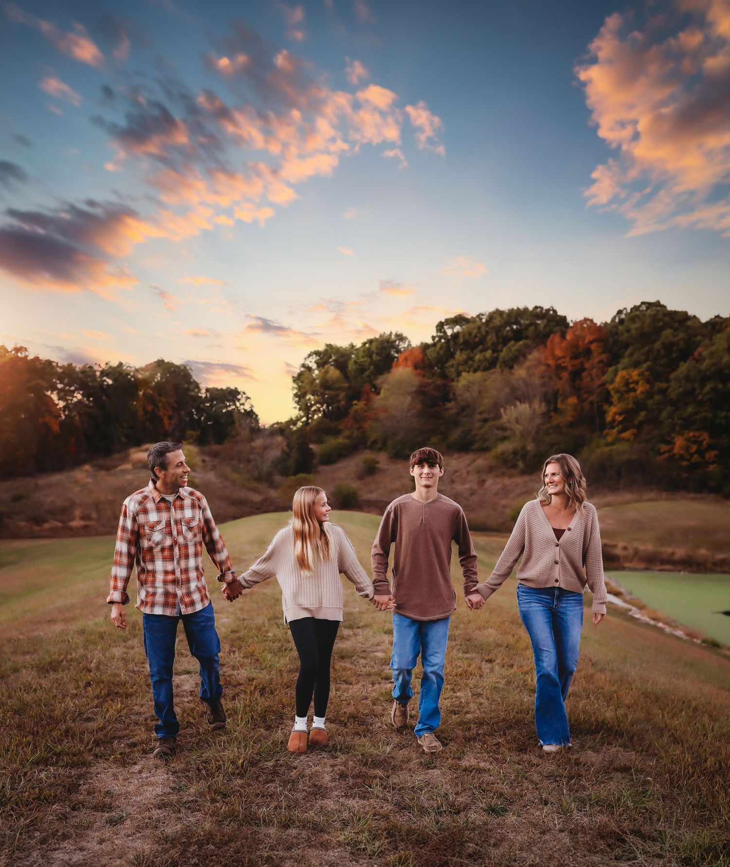 Back view of family members holding hands while walking at sunset on a hill.