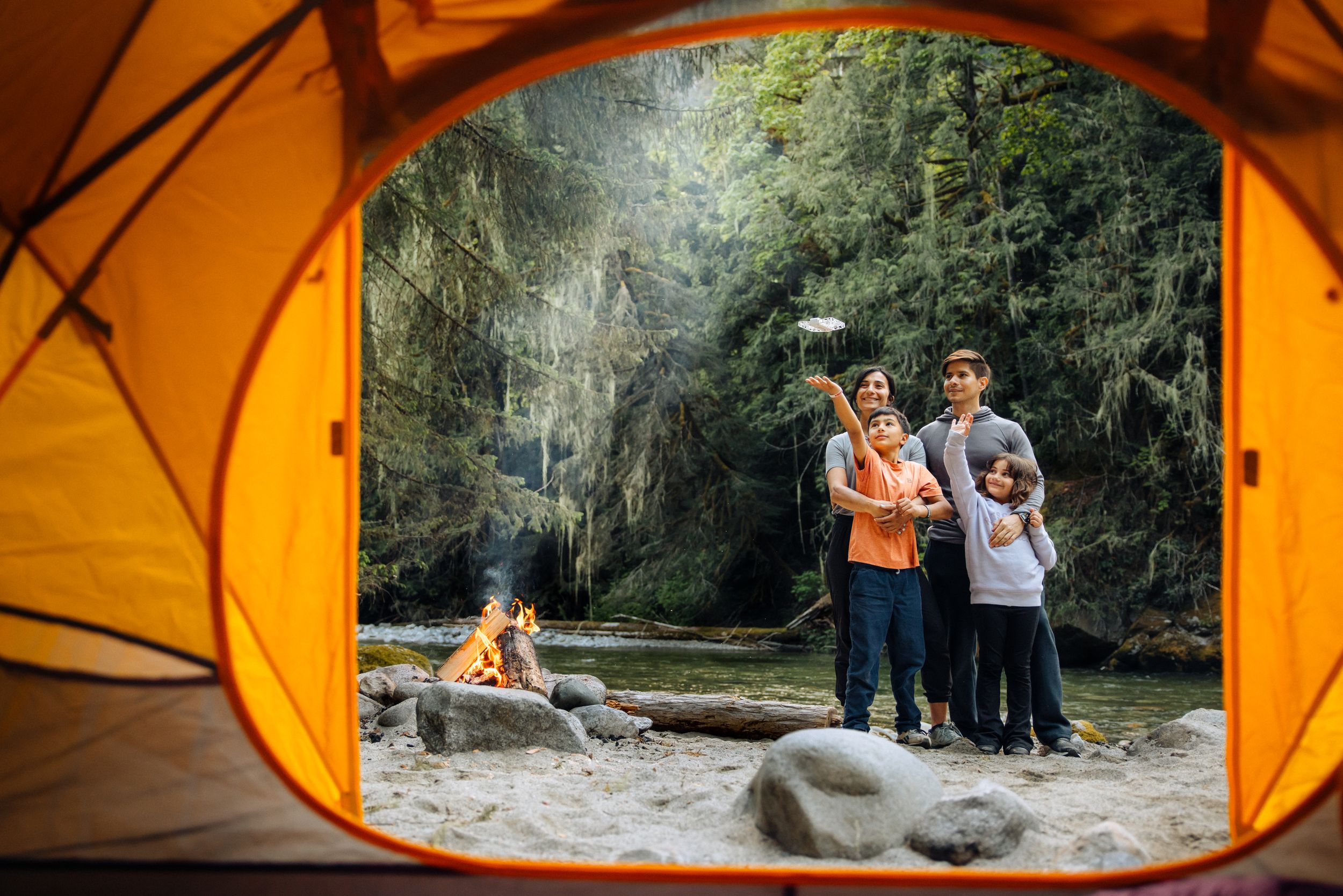 View through orange tent opening showing people enjoying scenic mountain landscape at sunset.