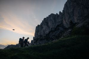 A silhouetted figure stands atop a rocky mountain ridge against a moody sunset sky.