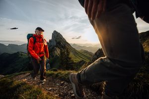 Hikers trek along rugged mountain ridge trail with dramatic mountain peaks in background.