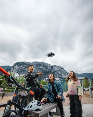 Group of friends point excitedly at something flying in the sky near a mountain landscape.