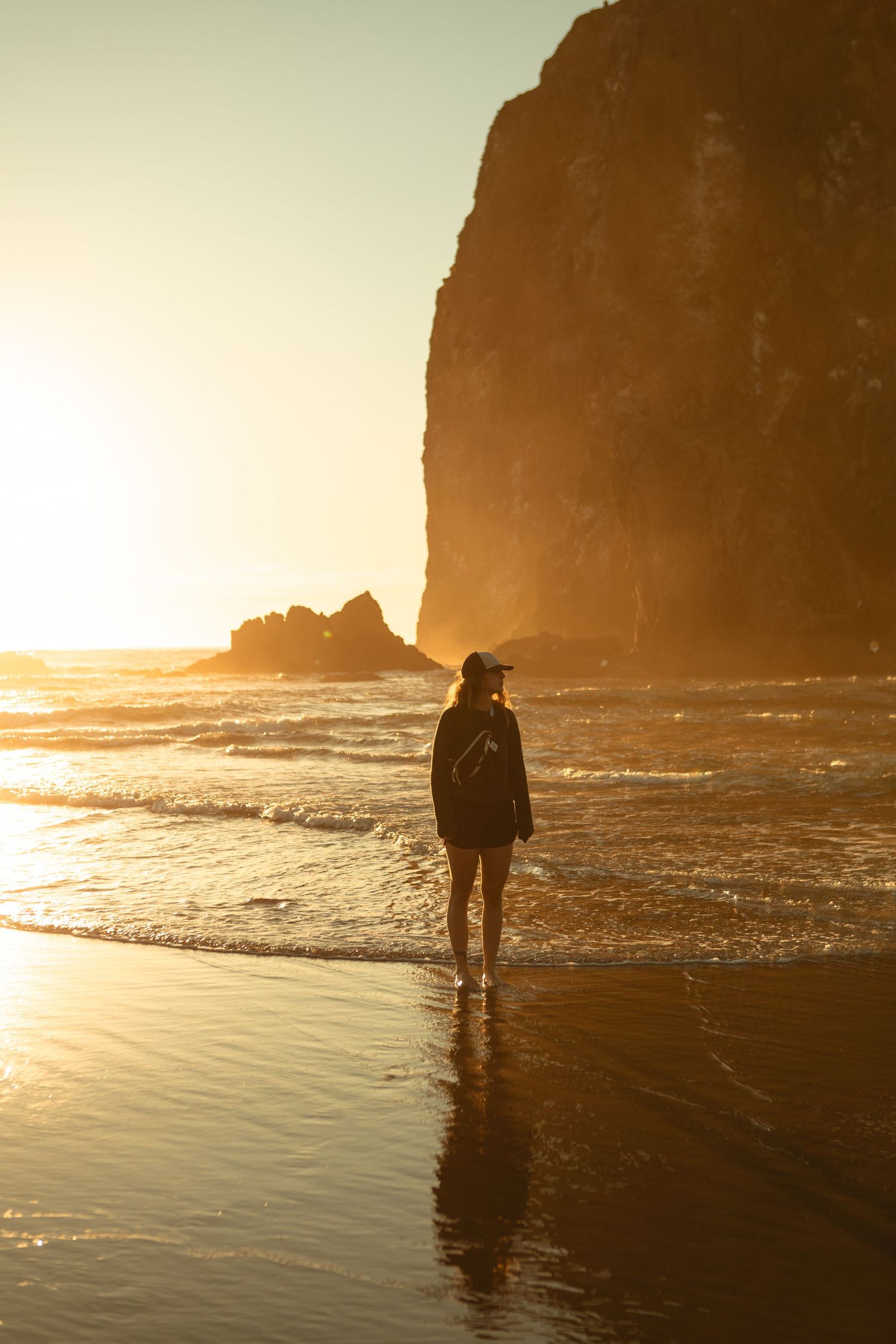 Elopement photographer - Silhouetted figure walks along misty beach at sunset with dramatic cliffs and golden reflections on wet sand.