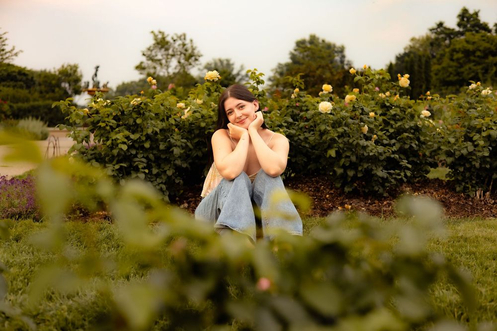 A person sits peacefully in a lush green meadow surrounded by wildflowers and trees on a sunny summer day.