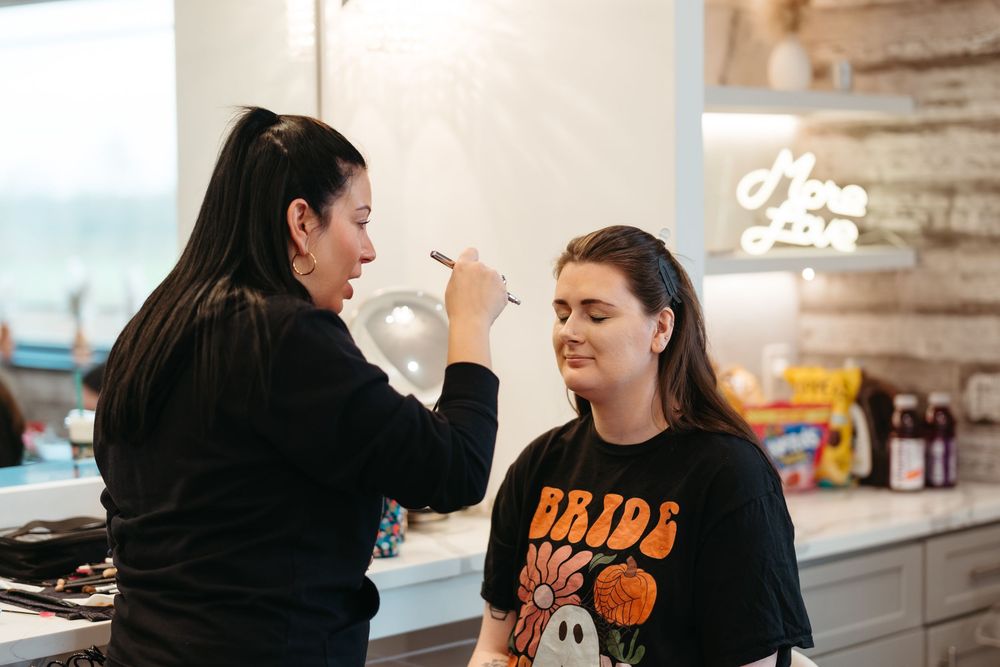 Professional makeup artist working on client's beauty preparation in a bright studio setting.