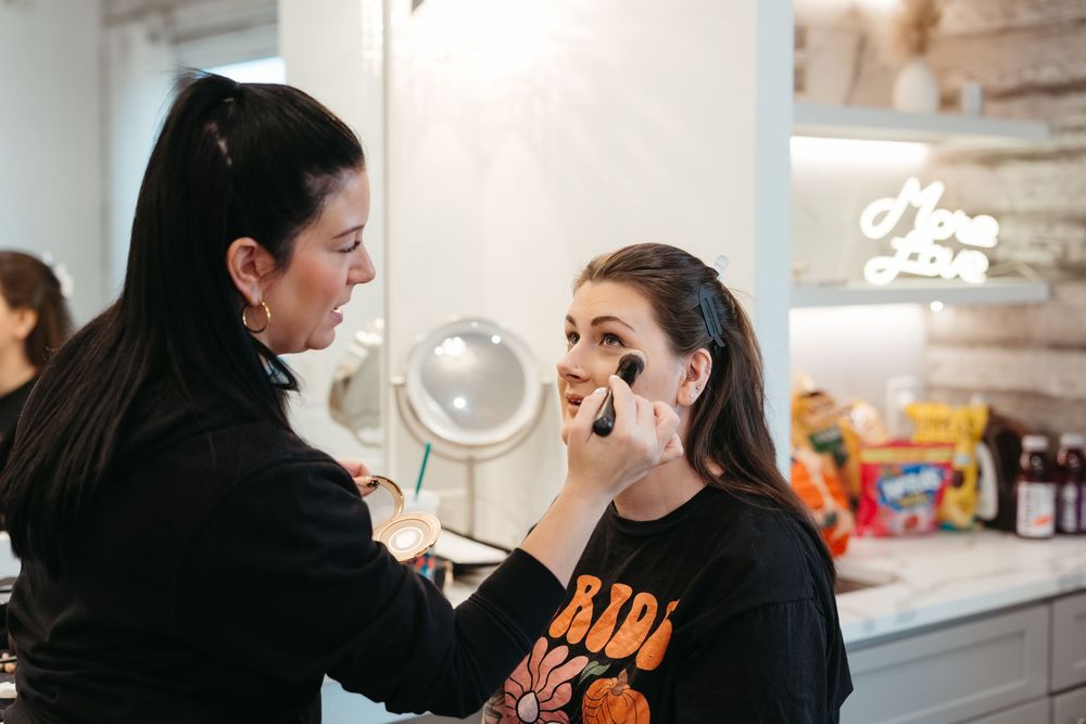 Makeup artist applying cosmetics during a beauty session in a well-lit room.