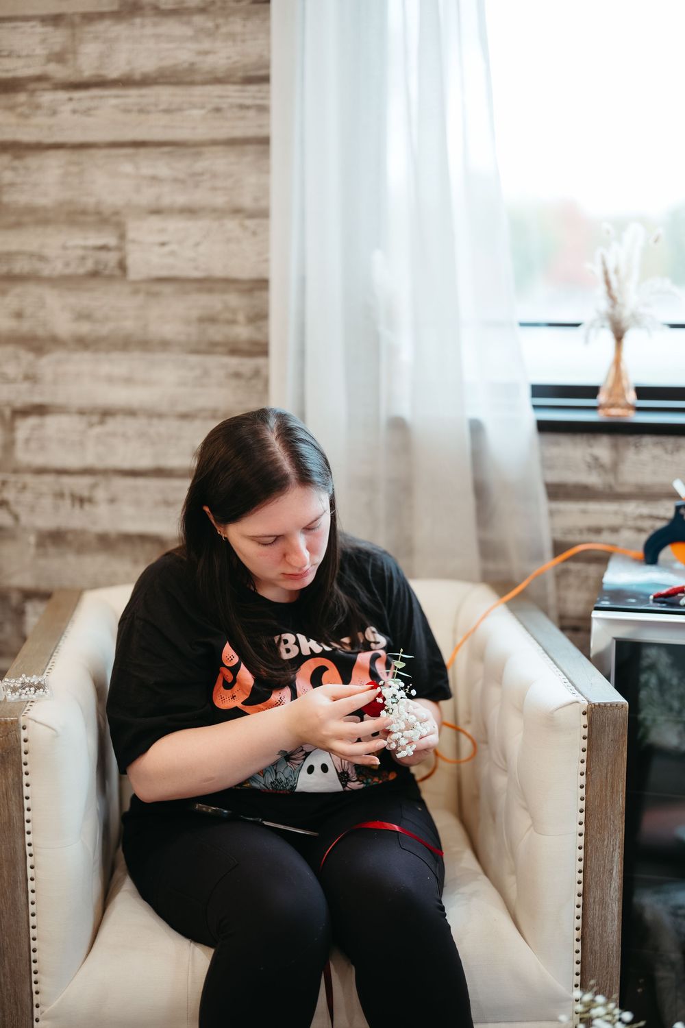 Someone sits on a cream-colored couch using a mobile device while wearing a black graphic t-shirt.