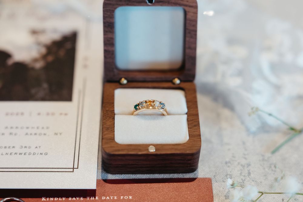 A sparkling engagement ring nestled in an elegant wooden box sits beside printed materials on a textured surface.