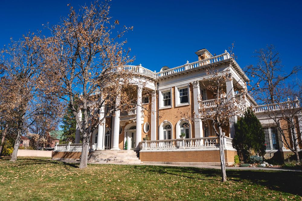 Historic mansion with tall white columns and ornate architecture set against bright blue sky in autumn.